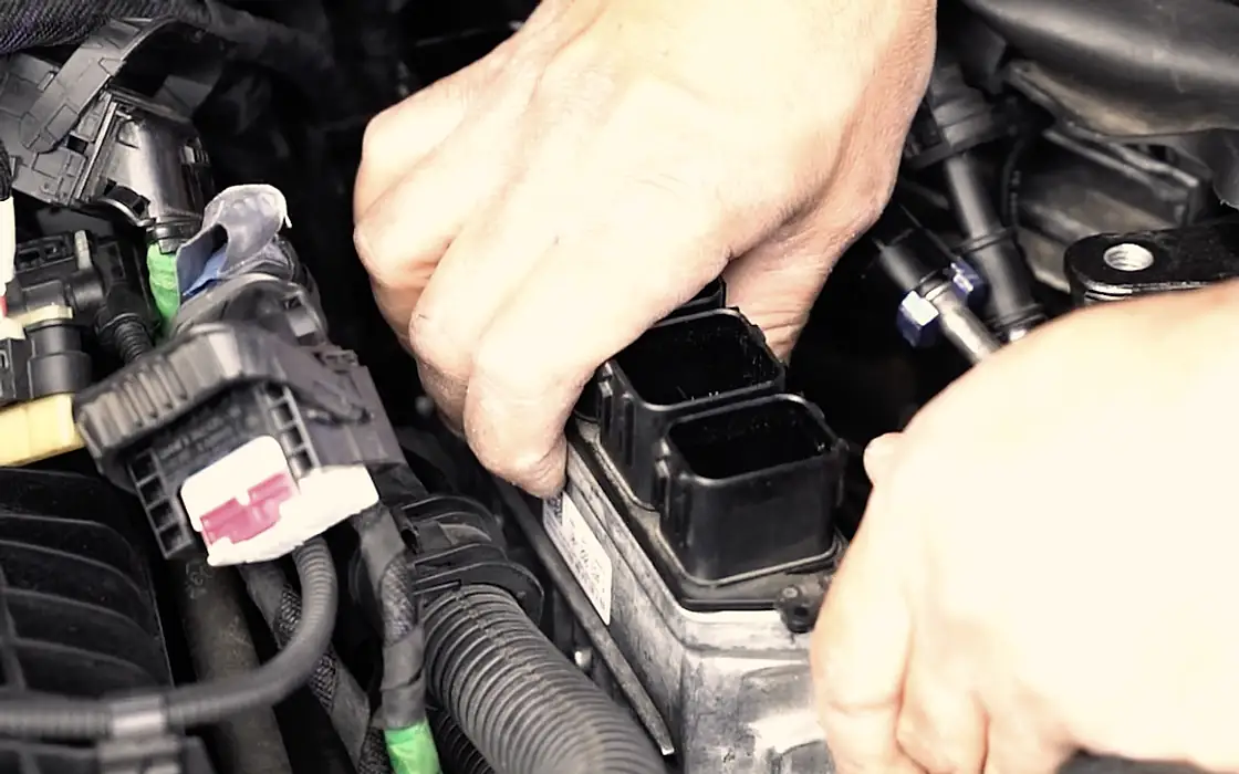 Hands unplugging the engine ECU connector in a customer's engine bay